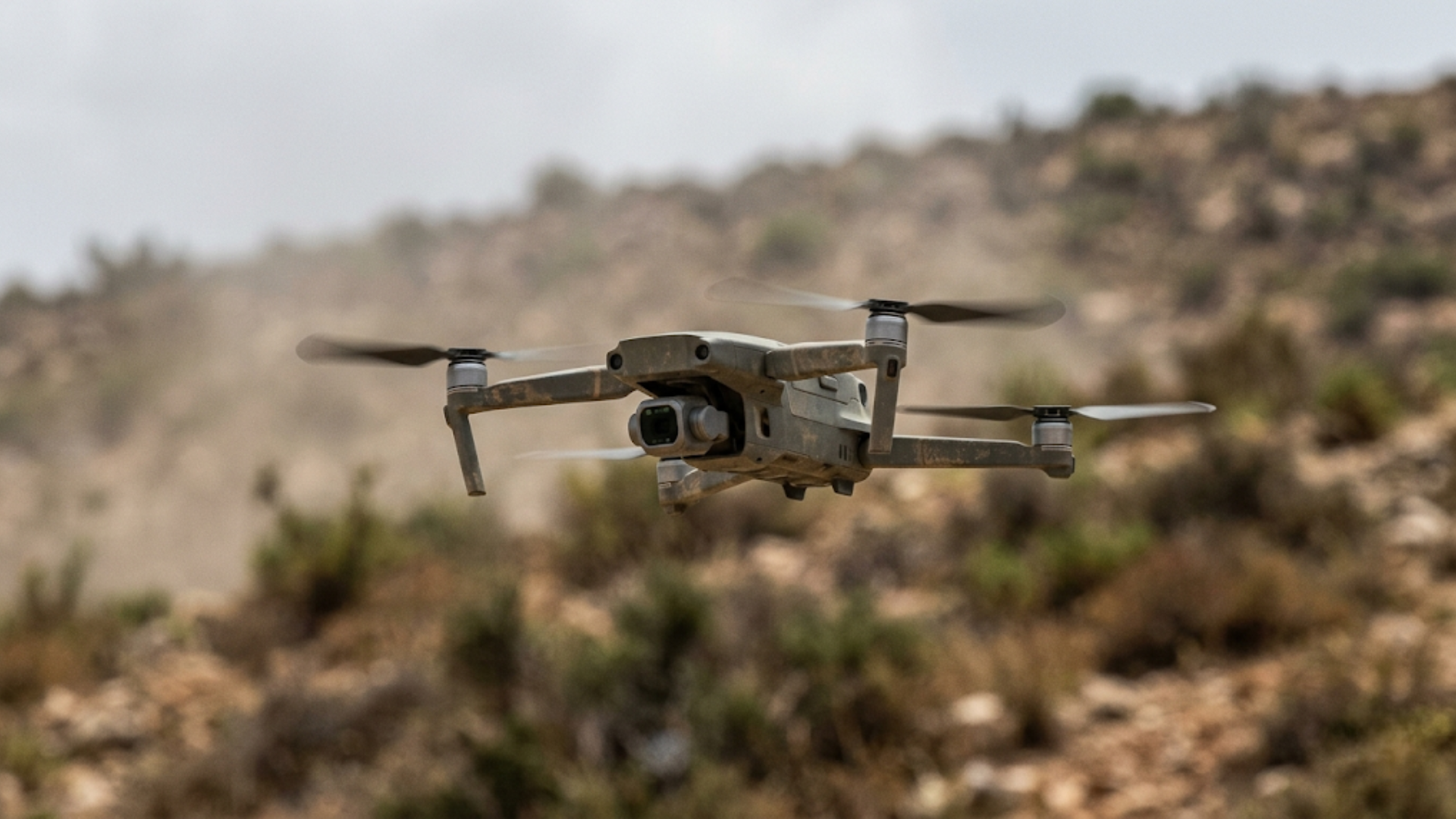 A military-grade drone flying over arid terrain in a live field environment.