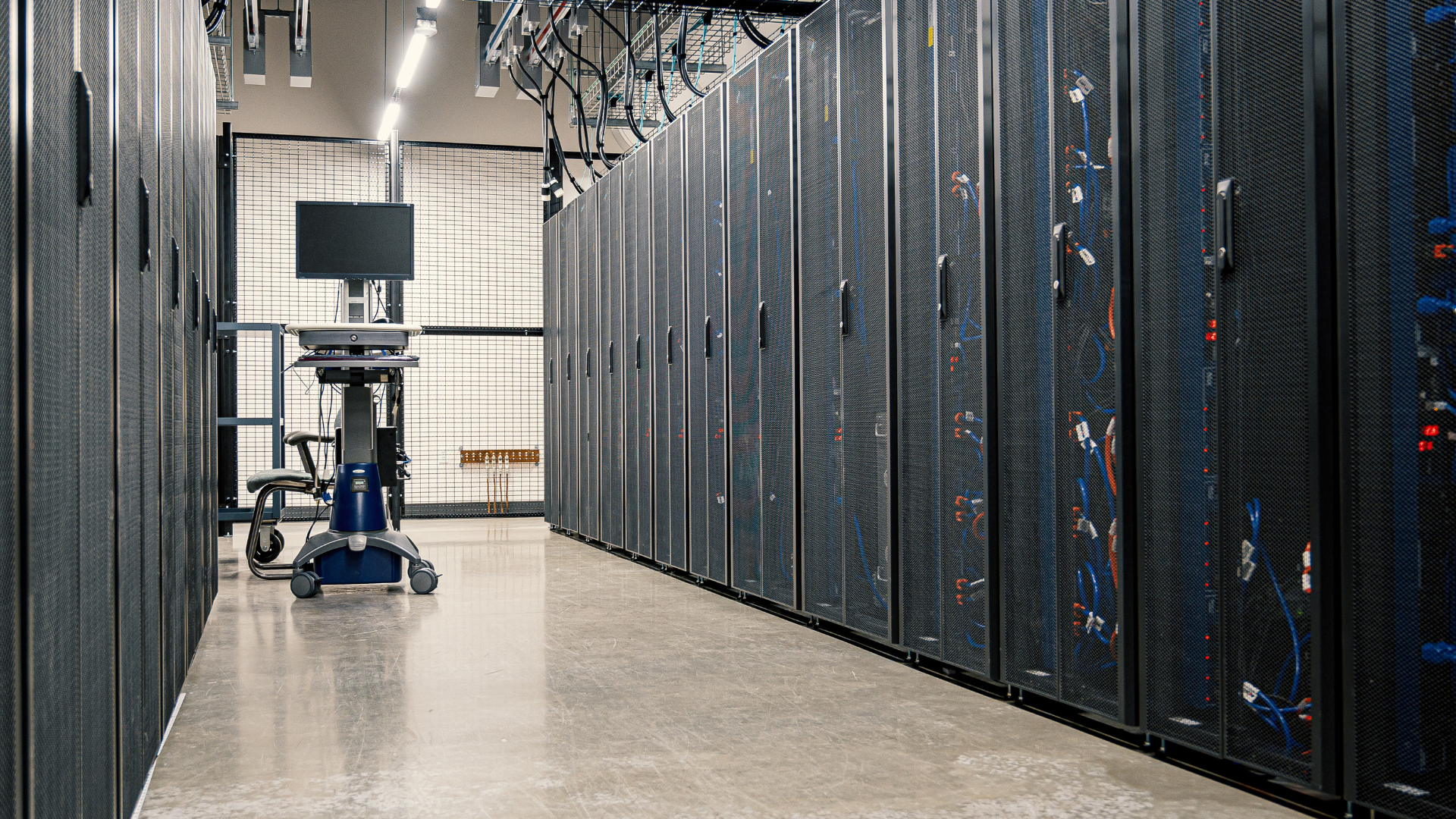 Server racks lining a data center aisle, the private compute and AI infrastructure that defense and robotics now rely on